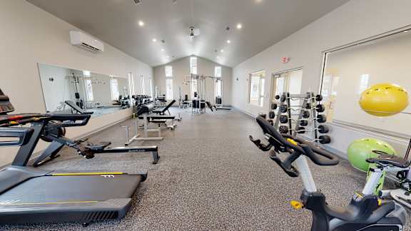 A gym with a variety of exercise equipment including treadmills, stationary bikes, and weight racks.