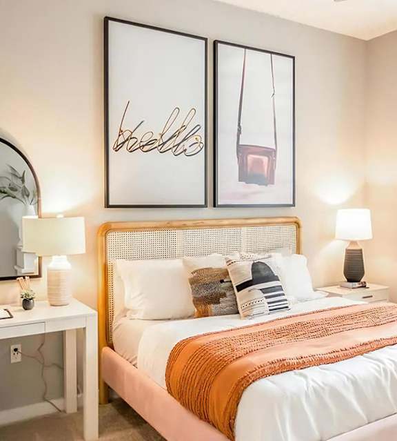 Bedroom with a cane headboard, framed prints, matching nightstand lamps, and a white desk beneath an arched mirror