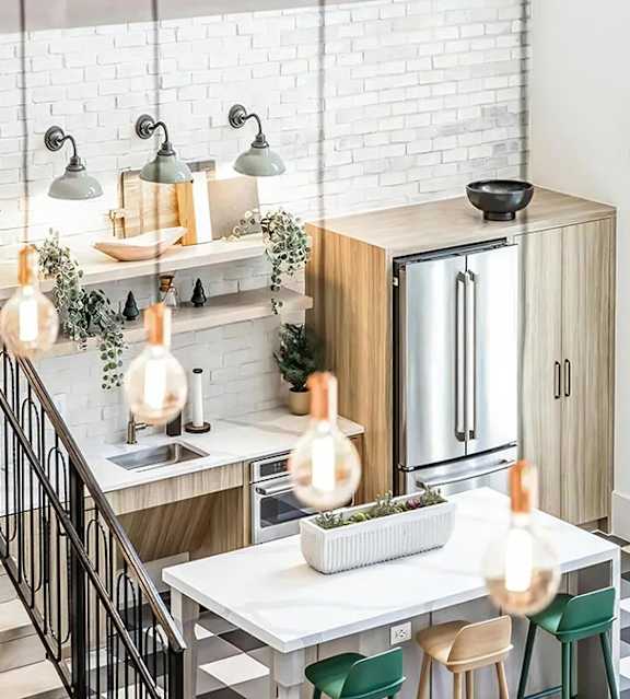Resident kitchen seen from above, with a white brick wall, open shelves under sconces, a refrigerator, an island and stools.