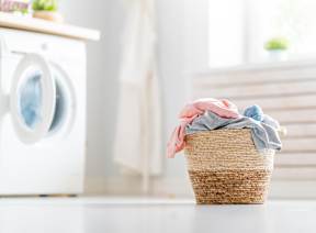 A basket with clothes is in front of a washing machine.