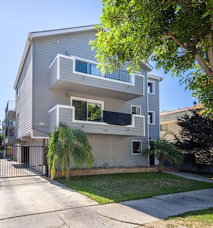 A modern two-story house with a white fence and a tree in front.