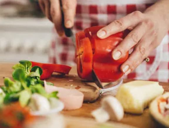 A person is cutting a red bell pepper on a wooden cutting board.