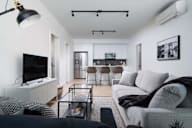A modern living room with a grey couch, a black and white patterned rug, and a television.