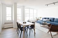 A dining table with four chairs and a sofa with a cushion in a room.