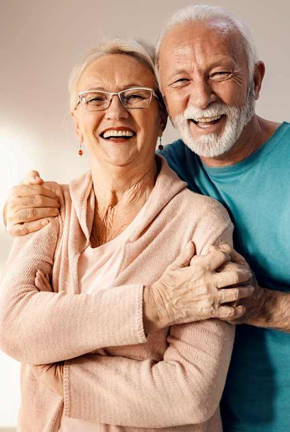 An elderly couple is hugging each other.