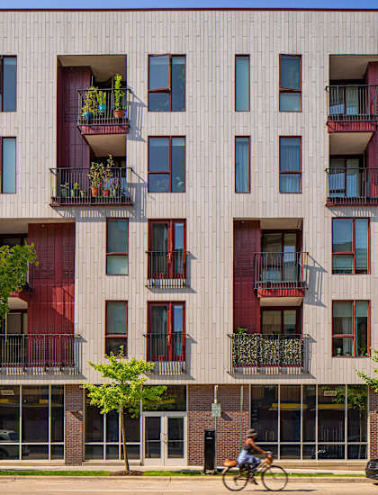 A person riding a bicycle in front of a building with balconies.