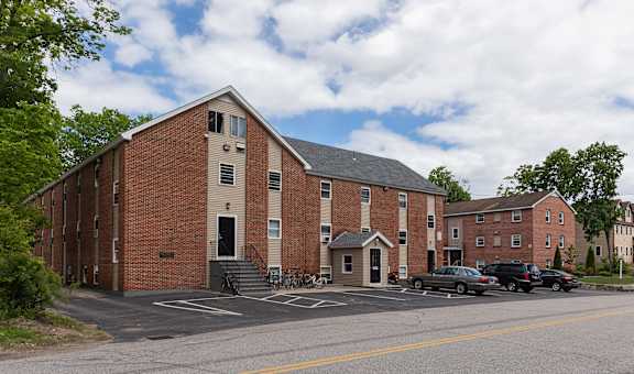 a large brick building with a gray roof and a parking lot in front of it