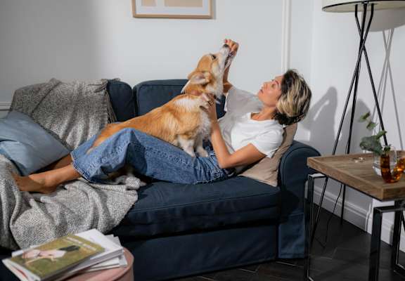 A woman is lying on a couch with her dog on her feet at Pines at Lawrenceville Apartments in Decatur, GA, 30033
