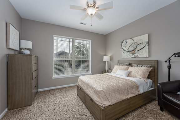 A bedroom with a large bed, a nightstand, and a window with white curtains.