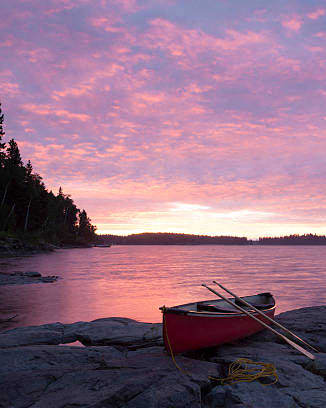 a red boat sitting on a rock next to the water