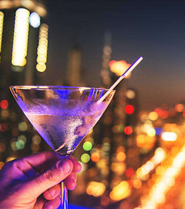 A hand holding a martini glass with a cityscape at night in the background.