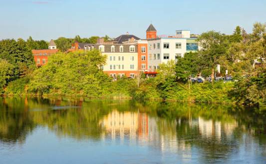 A serene lake reflects the buildings and trees around it.