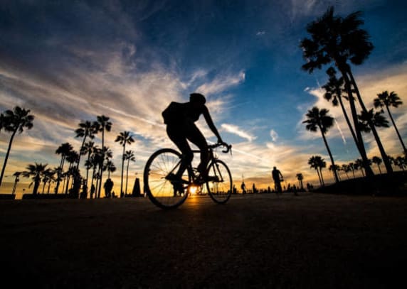 a man riding a bike down a street at sunset