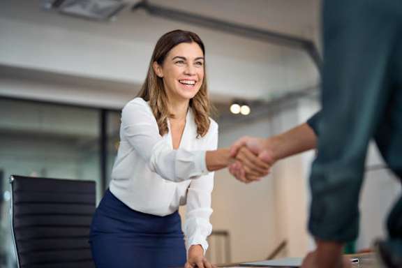 A woman in a white shirt and blue skirt shakes hands with a man in a green shirt.