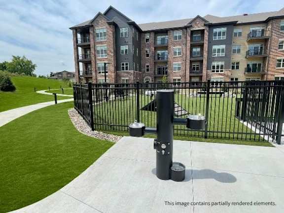 A black metal fence surrounds a grassy area in front of a brick apartment building.