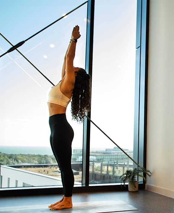 Two women practicing yoga in a bright room with large windows.