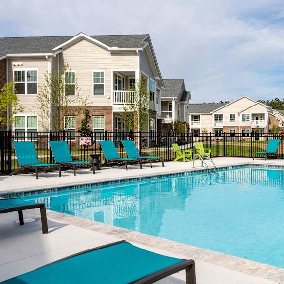 A swimming pool with lounge chairs and a fence in front of apartment buildings.