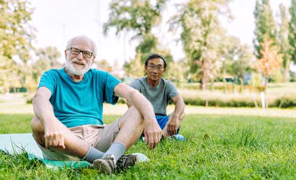 Two men sitting on a green mat in a park.