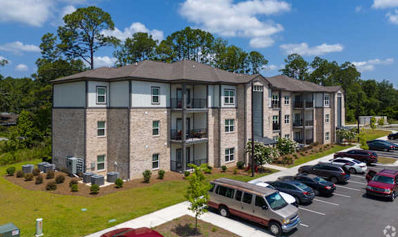 A parking lot in front of a building with a red car in the foreground. at Arbours at Kingsland, Kingsland, Georgia