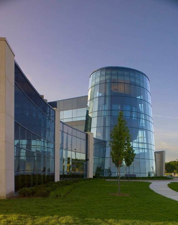A modern glass building with a curved facade and a tree in front.