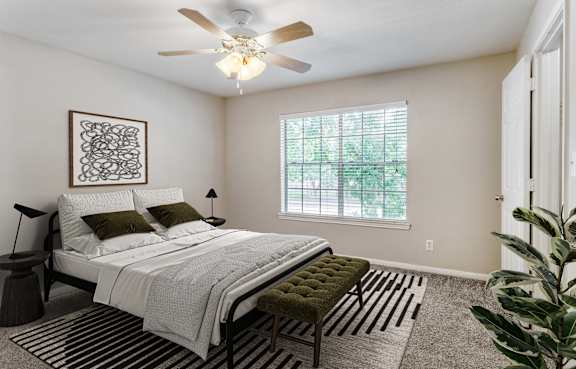 A bedroom with a bed, a bench, and a ceiling fan.