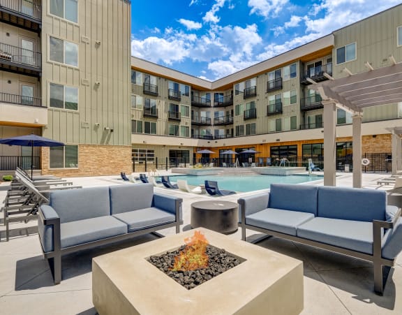 a patio with couches and a fire pit with a pool in the background