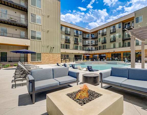 a poolside lounge area with chairs and a fire pit in front of a building