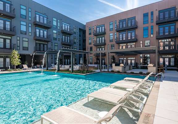 a swimming pool with lounge chairs and umbrellas in front of an apartment building