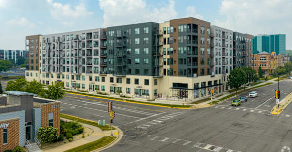 A large apartment building is situated on a street corner with a traffic light and a crosswalk.