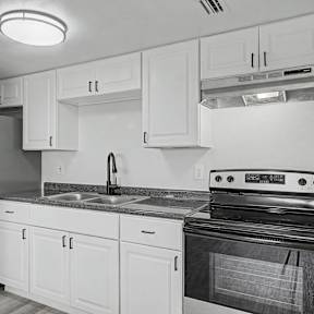 A black and white photo of a kitchen with white cabinets and a black stove.