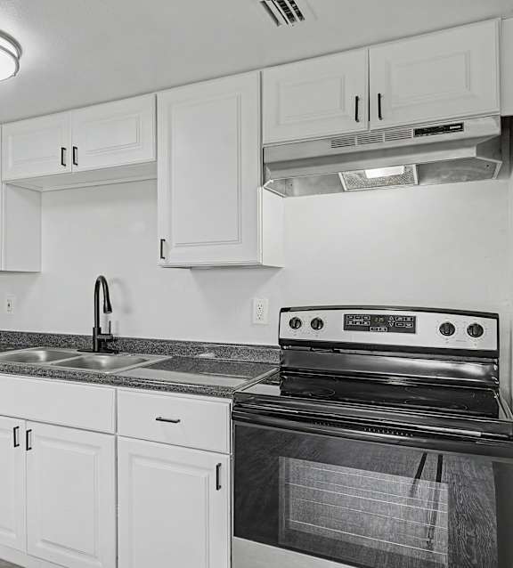 A black and white photo of a kitchen with white cabinets and a black stove.