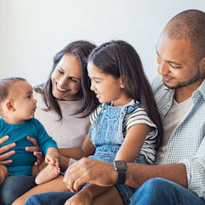 A family of four is sitting together on a bed.