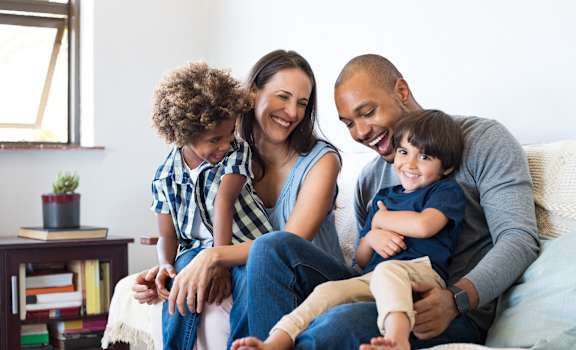 A family of four is sitting on a couch together.