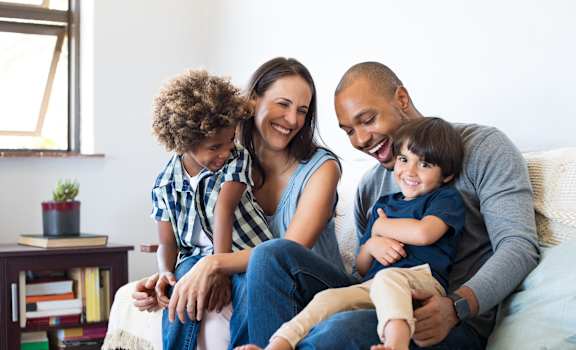 A family of four is sitting on a couch together.