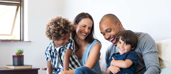 A family of four is sitting on a couch together.