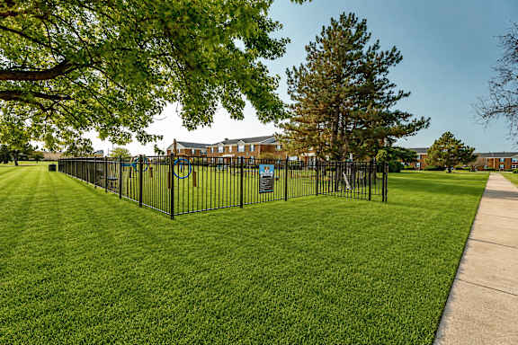 A black fence surrounds a green lawn with a building in the background.
