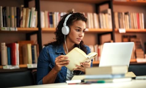 a woman with headphones and a book in front of a laptop