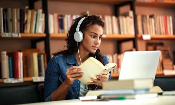 a woman with headphones and a book in front of a laptop