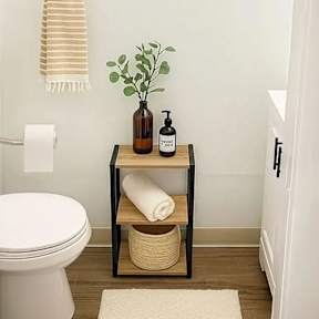 A bathroom with a toilet, a table with a plant and toiletries on it, and a towel hanging on a towel ring.