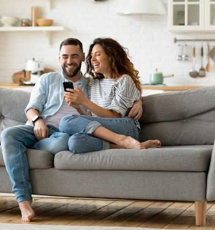 a man and woman sitting on a couch looking at a cell phone