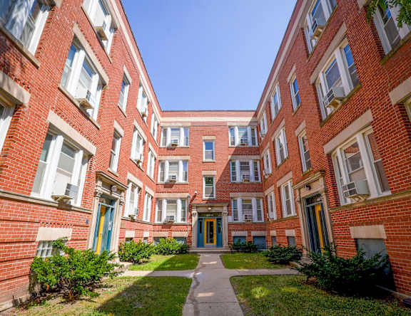 A long hallway with red brick buildings and green bushes on the side.