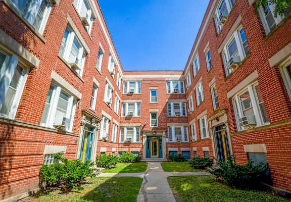 A long hallway between red brick buildings with green bushes on the sides.