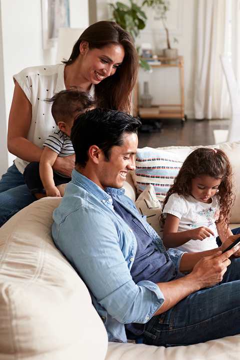A family of four is sitting on a couch at Northridge Gardens Apartments, Northridge, CA