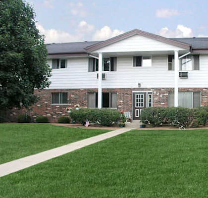 A white house with a brick wall and a green lawn in front.