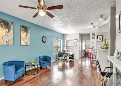 A living room with blue chairs and a ceiling fan.