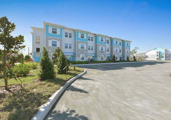 A modern apartment building with a parking lot in front.at Allegra at Cocoa in Cocoa, FL, 32926