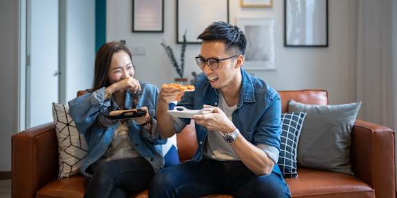 Two people sitting on a couch eating pizza.