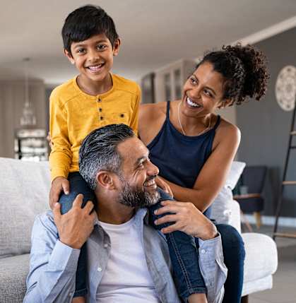 A family of three is sitting on a couch in a living room.