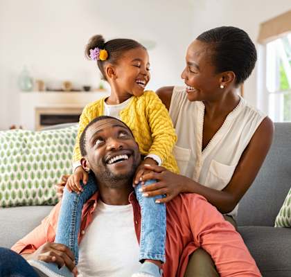 A family of three is sitting on a couch, with the child on the man's shoulders.