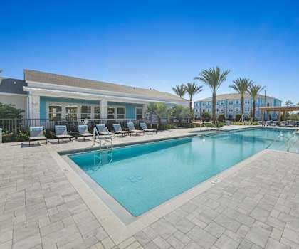 A swimming pool surrounded by a tiled patio and lounge chairs.